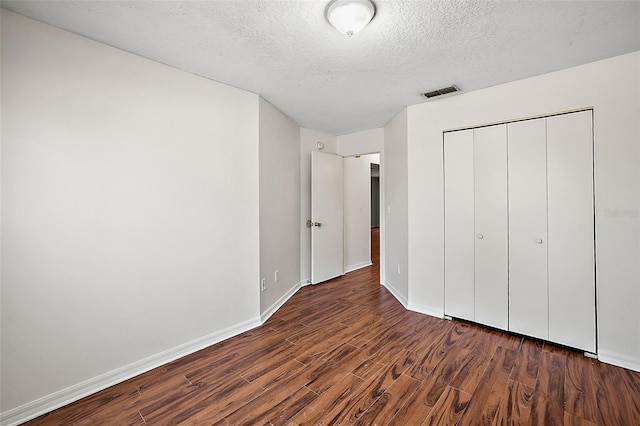 unfurnished bedroom featuring a textured ceiling, a closet, and dark hardwood / wood-style flooring