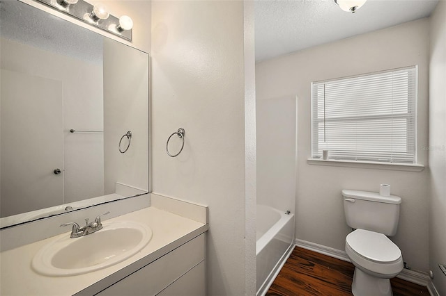 bathroom with toilet, vanity, a tub, wood-type flooring, and a textured ceiling