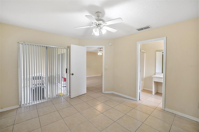 unfurnished bedroom with ceiling fan, connected bathroom, light tile patterned floors, and a textured ceiling