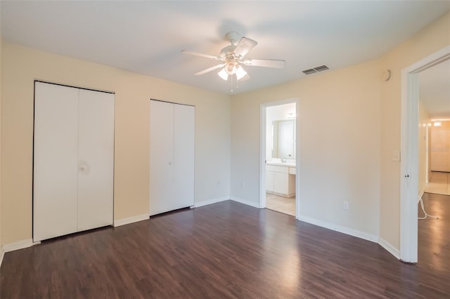 unfurnished bedroom featuring ceiling fan, dark hardwood / wood-style floors, connected bathroom, and two closets