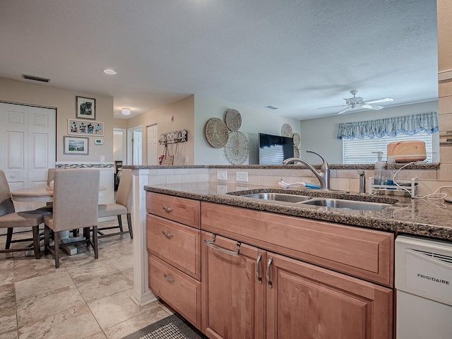 kitchen featuring ceiling fan, dark stone countertops, dishwasher, and sink