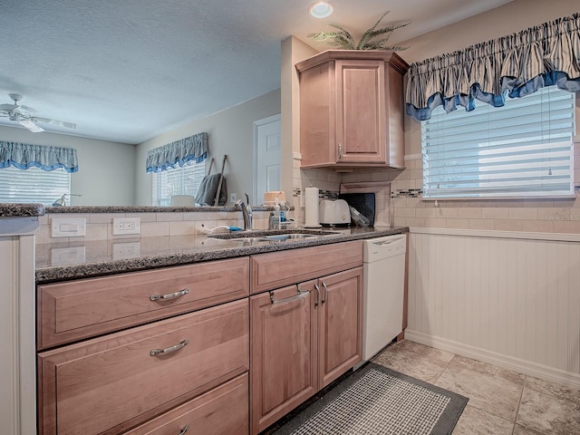 kitchen featuring dishwasher, light brown cabinets, dark stone countertops, sink, and ceiling fan