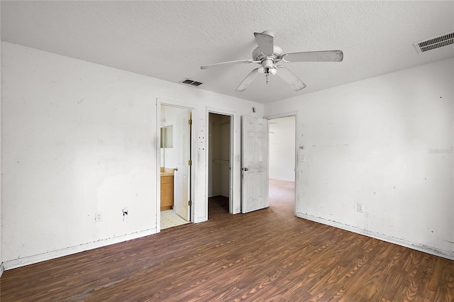 unfurnished bedroom with ceiling fan, ensuite bath, a textured ceiling, a walk in closet, and dark hardwood / wood-style flooring