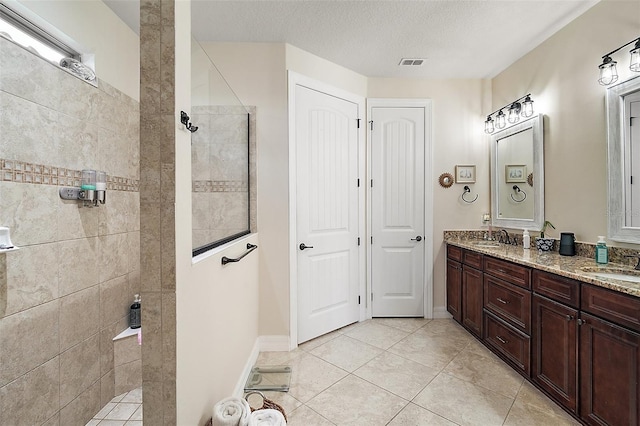 bathroom with a textured ceiling, vanity, a tile shower, and tile patterned flooring