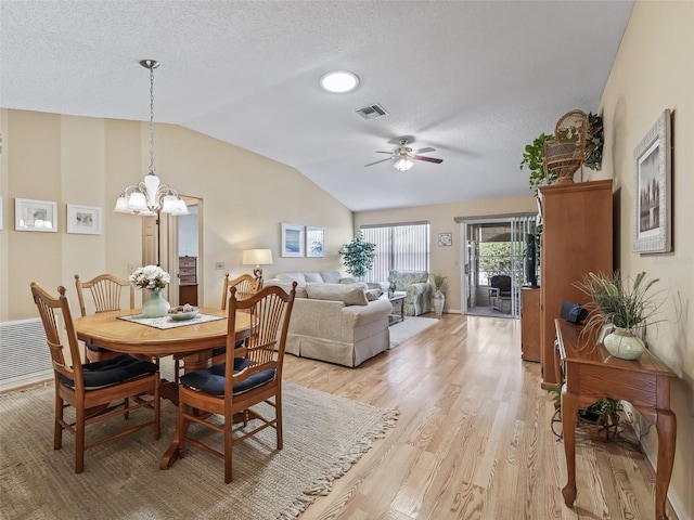 dining room with vaulted ceiling, ceiling fan with notable chandelier, a textured ceiling, and light hardwood / wood-style flooring