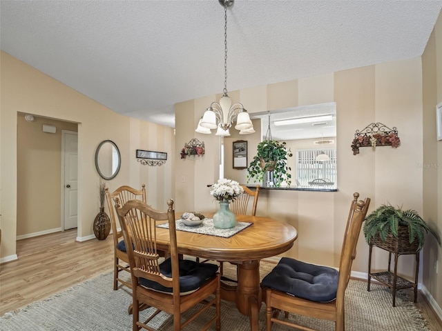 dining room with a notable chandelier, lofted ceiling, light hardwood / wood-style flooring, and a textured ceiling