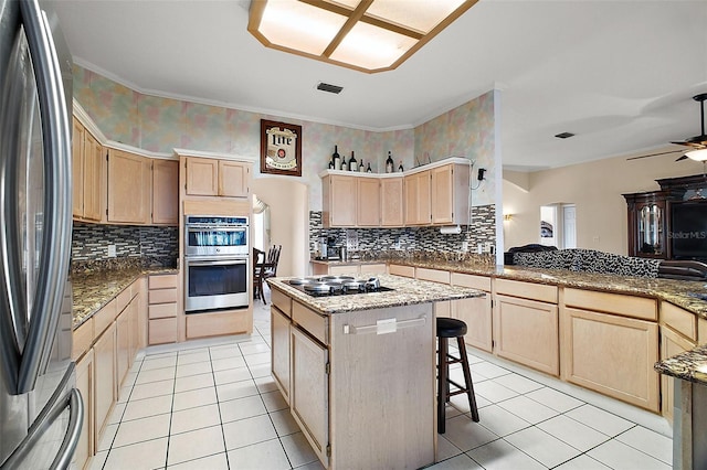 kitchen with appliances with stainless steel finishes, a center island, light brown cabinets, ceiling fan, and a breakfast bar area