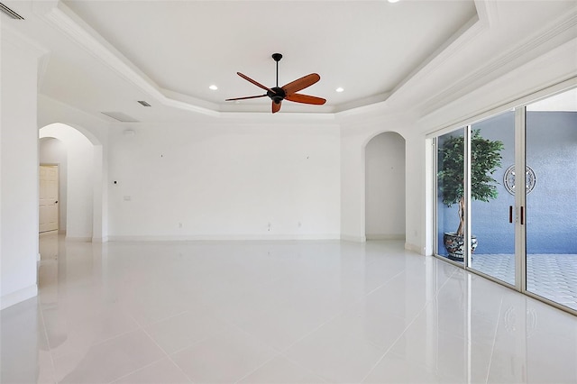 empty room with ceiling fan, a raised ceiling, crown molding, and light tile patterned flooring