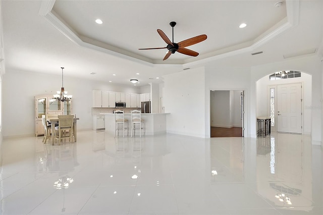 unfurnished living room featuring ceiling fan with notable chandelier, a raised ceiling, crown molding, and light tile patterned flooring