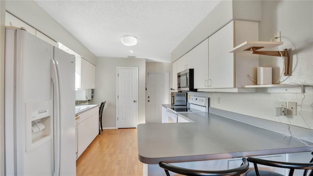 kitchen with white cabinetry, a textured ceiling, white appliances, and light hardwood / wood-style floors