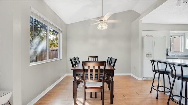 dining space with ceiling fan, lofted ceiling, sink, and light wood-type flooring