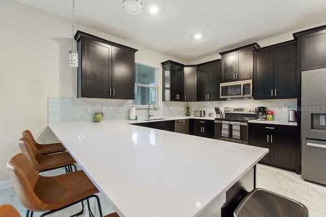 kitchen featuring stainless steel appliances, tasteful backsplash, hanging light fixtures, a breakfast bar, and sink