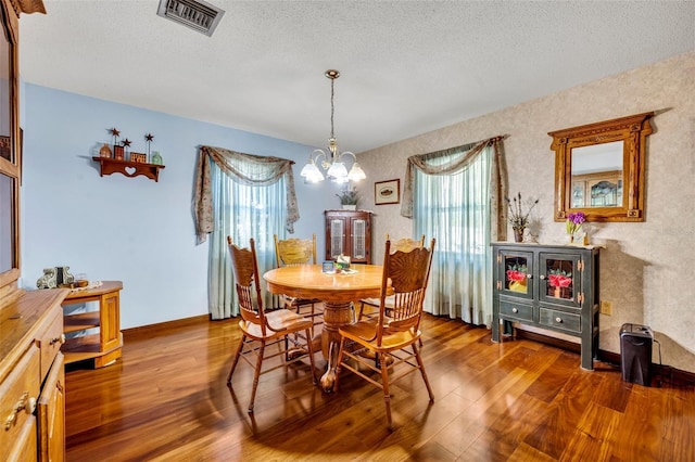 dining area with wood-type flooring, a wealth of natural light, a notable chandelier, and a textured ceiling