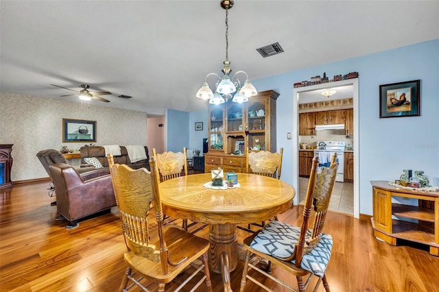 dining space with ceiling fan with notable chandelier and light hardwood / wood-style flooring