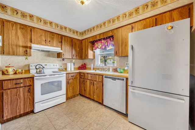 kitchen featuring sink, white appliances, light tile patterned floors, and a textured ceiling