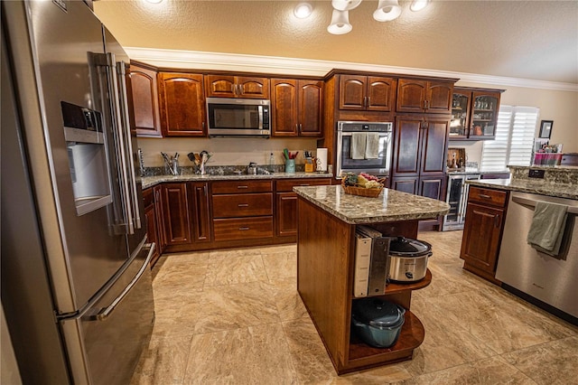 kitchen featuring a textured ceiling, appliances with stainless steel finishes, a kitchen island, stone countertops, and ornamental molding