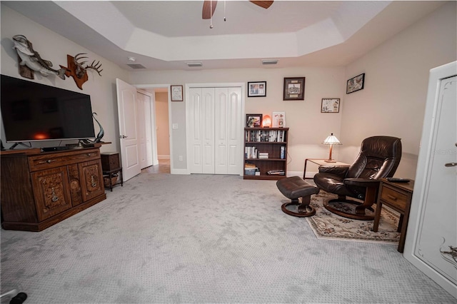 sitting room featuring ceiling fan, light carpet, and a raised ceiling