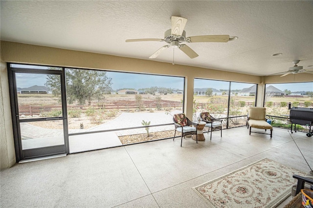 unfurnished sunroom with ceiling fan, a wealth of natural light, and a rural view