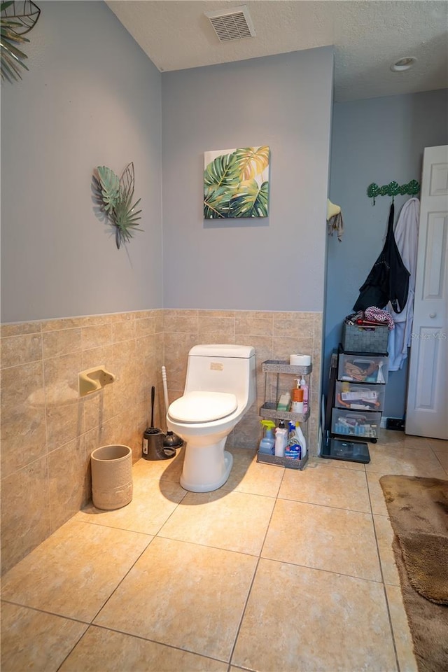 bathroom featuring toilet, tile patterned flooring, and tile walls