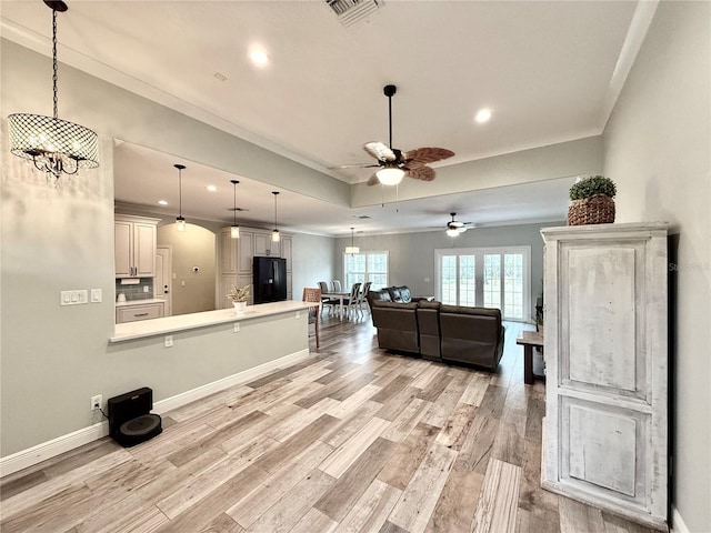 kitchen with black refrigerator, pendant lighting, light hardwood / wood-style floors, a tray ceiling, and crown molding