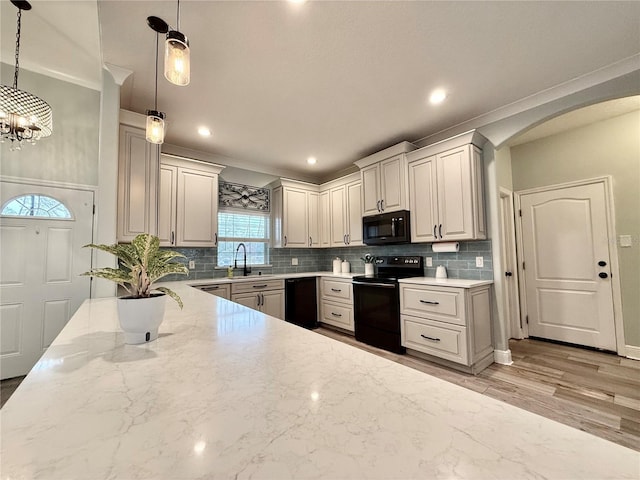 kitchen with sink, light stone countertops, black appliances, decorative backsplash, and decorative light fixtures