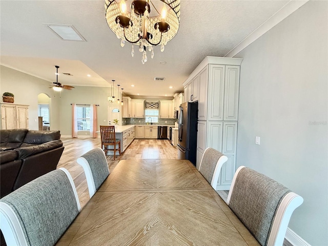 dining space with crown molding, sink, ceiling fan with notable chandelier, and light hardwood / wood-style floors