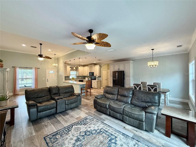 living room with ornamental molding, ceiling fan with notable chandelier, a textured ceiling, and light wood-type flooring