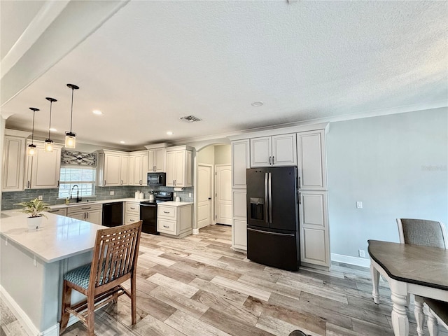 kitchen featuring black appliances, decorative backsplash, hanging light fixtures, kitchen peninsula, and light wood-type flooring