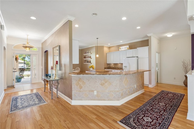 kitchen with white cabinetry, crown molding, decorative light fixtures, light stone countertops, and white refrigerator with ice dispenser