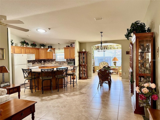 dining space with light tile patterned flooring, lofted ceiling, and ceiling fan with notable chandelier