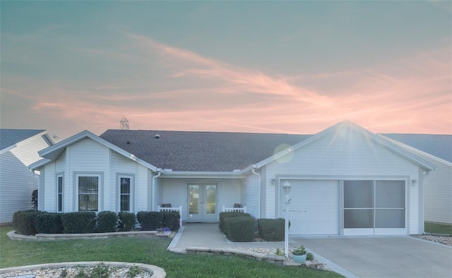 ranch-style home featuring an attached garage, a shingled roof, driveway, french doors, and a lawn