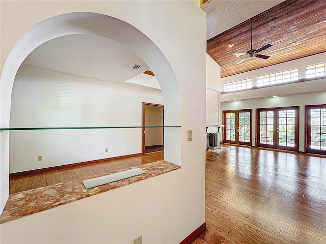 empty room with wood ceiling, ceiling fan, a high ceiling, wood-type flooring, and french doors