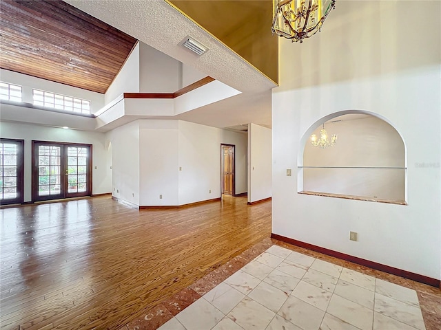 empty room featuring wooden ceiling, french doors, a chandelier, and a high ceiling