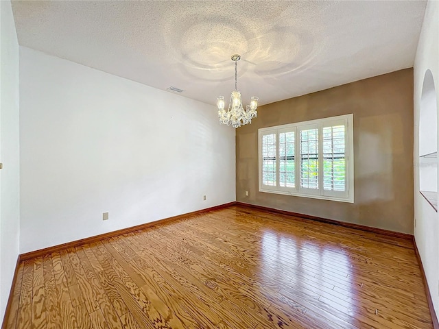 spare room featuring wood-type flooring, a textured ceiling, and an inviting chandelier