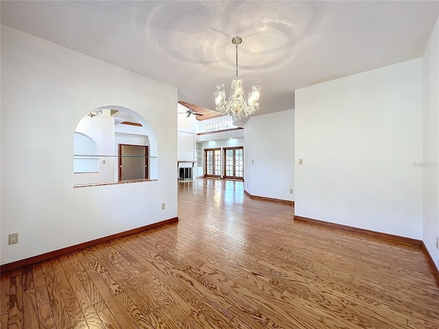 empty room with wood-type flooring, ceiling fan with notable chandelier, and a textured ceiling