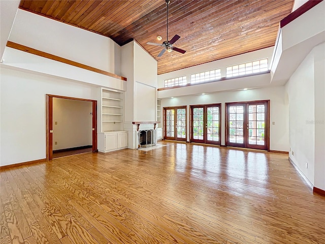 unfurnished living room featuring french doors, a high ceiling, wood ceiling, light wood-type flooring, and built in shelves