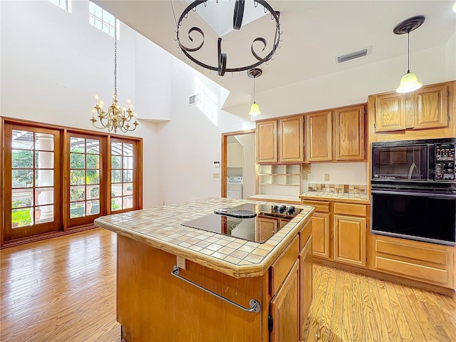 kitchen with tile counters, a center island, light wood-type flooring, and black appliances