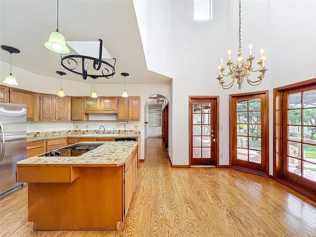 kitchen with a towering ceiling, decorative light fixtures, stainless steel refrigerator, and a center island