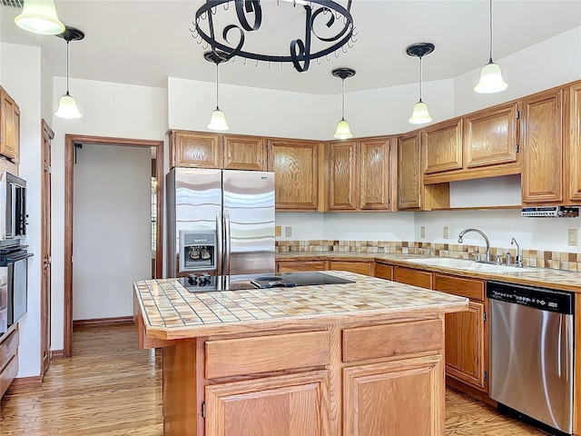 kitchen with sink, light hardwood / wood-style flooring, appliances with stainless steel finishes, a kitchen island, and tile countertops