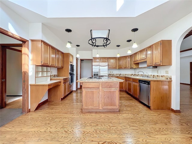 kitchen with sink, appliances with stainless steel finishes, a center island, decorative light fixtures, and light wood-type flooring