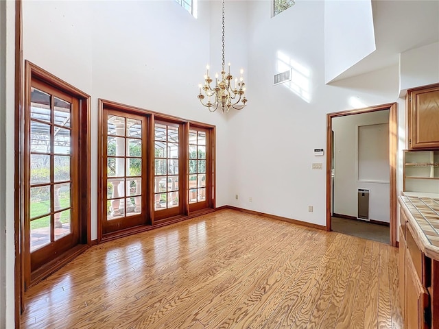 unfurnished dining area with a high ceiling, plenty of natural light, an inviting chandelier, and light wood-type flooring