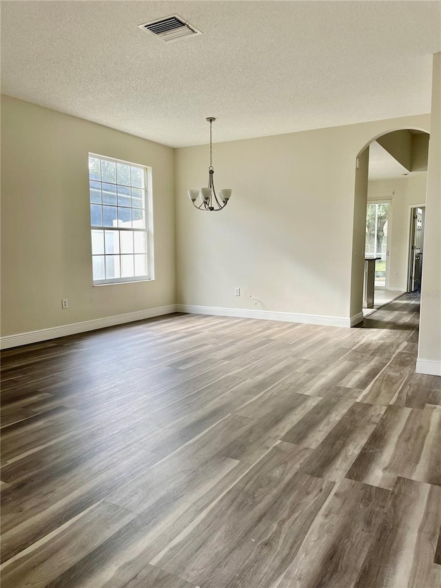 empty room featuring dark hardwood / wood-style flooring, a chandelier, and a textured ceiling