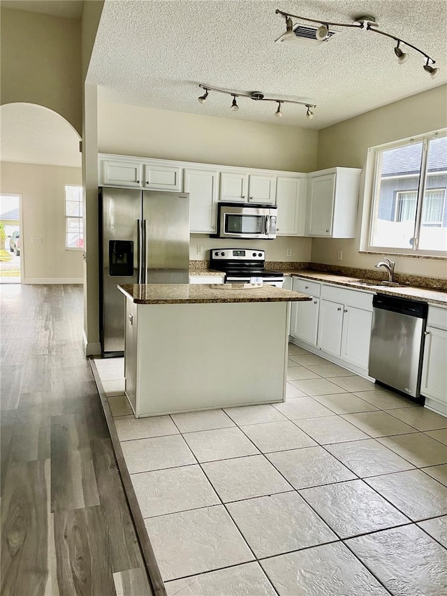 kitchen featuring white cabinetry, stainless steel appliances, dark stone counters, a textured ceiling, and a kitchen island