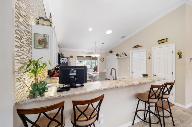 kitchen featuring kitchen peninsula, decorative backsplash, a kitchen bar, crown molding, and light stone counters