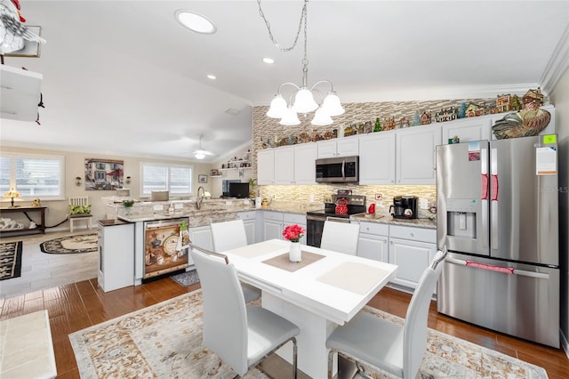 kitchen featuring kitchen peninsula, appliances with stainless steel finishes, hanging light fixtures, vaulted ceiling, and ornamental molding