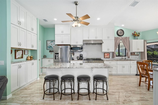 kitchen with a kitchen island, appliances with stainless steel finishes, sink, white cabinets, and light stone countertops