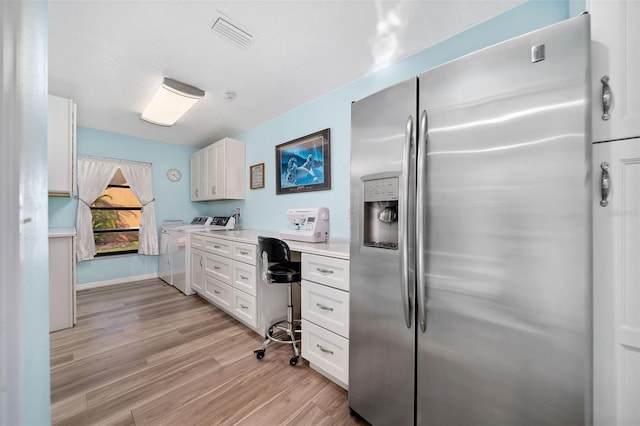 kitchen with washing machine and clothes dryer, white cabinetry, built in desk, stainless steel fridge with ice dispenser, and light hardwood / wood-style flooring