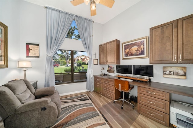 home office featuring hardwood / wood-style flooring, built in desk, ceiling fan, and a towering ceiling