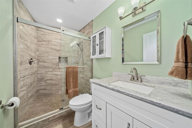 bathroom with a shower with door, vanity, wood-type flooring, and toilet