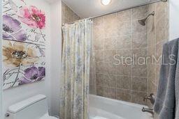 bathroom featuring toilet and shower / bathtub combination with curtain